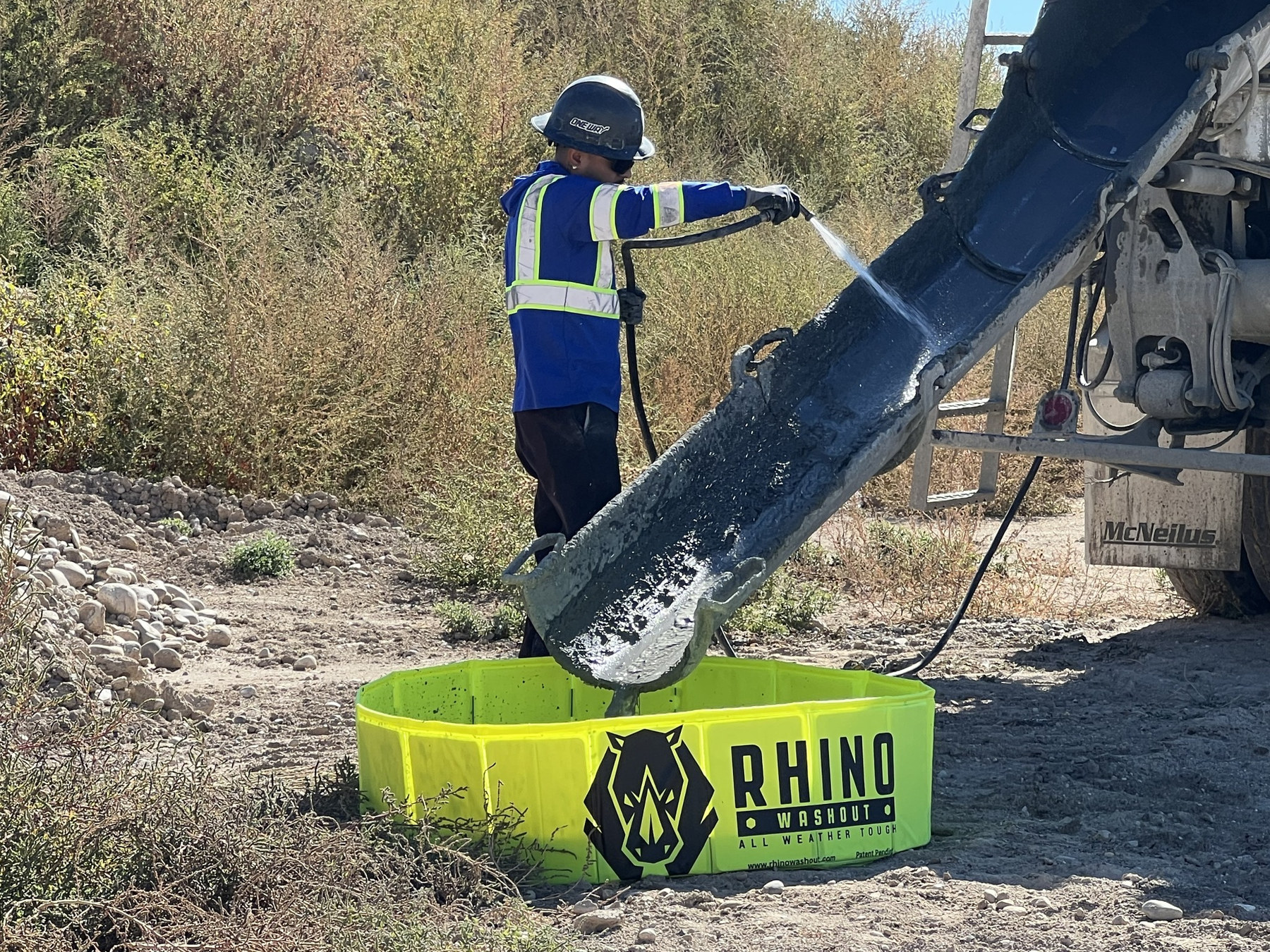 Worker washing a concrete truck chute into a Rhino Washout on a jobsite